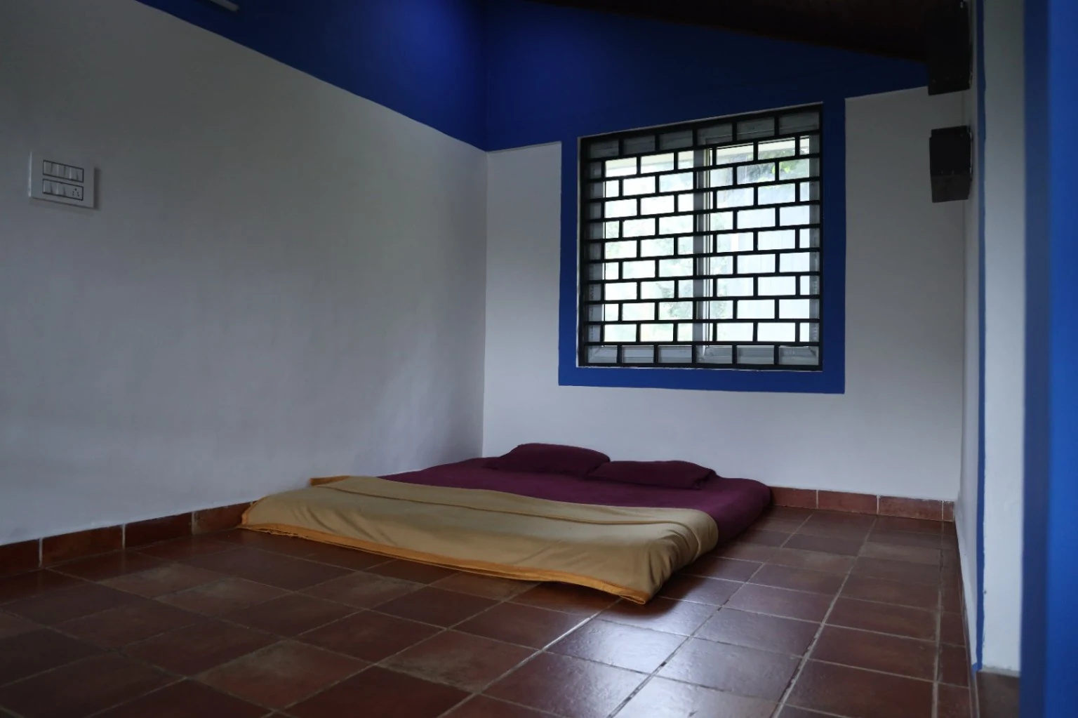 Simple bedding on a tiled floor beside a barred window