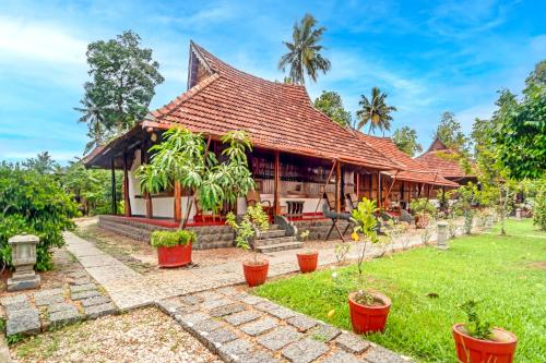 Illustrative property imagery: a traditional Kerala heritage home with a steep tiled roof, timber verandah and potted plants along a stone path