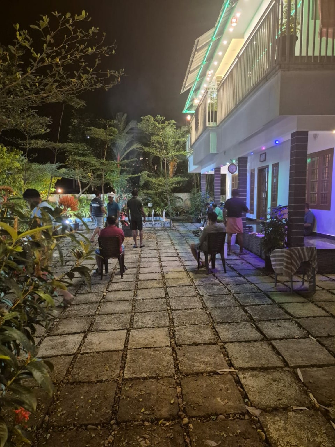 The courtyard at Dense Villa in the evening, guests seated on chairs beneath a lit balcony