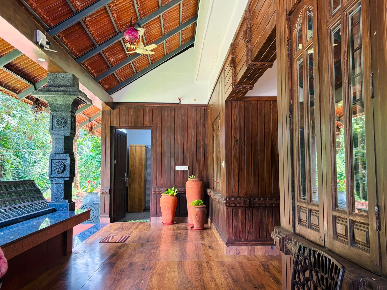 A wide wooden verandah with seating, looking out over a Kerala garden