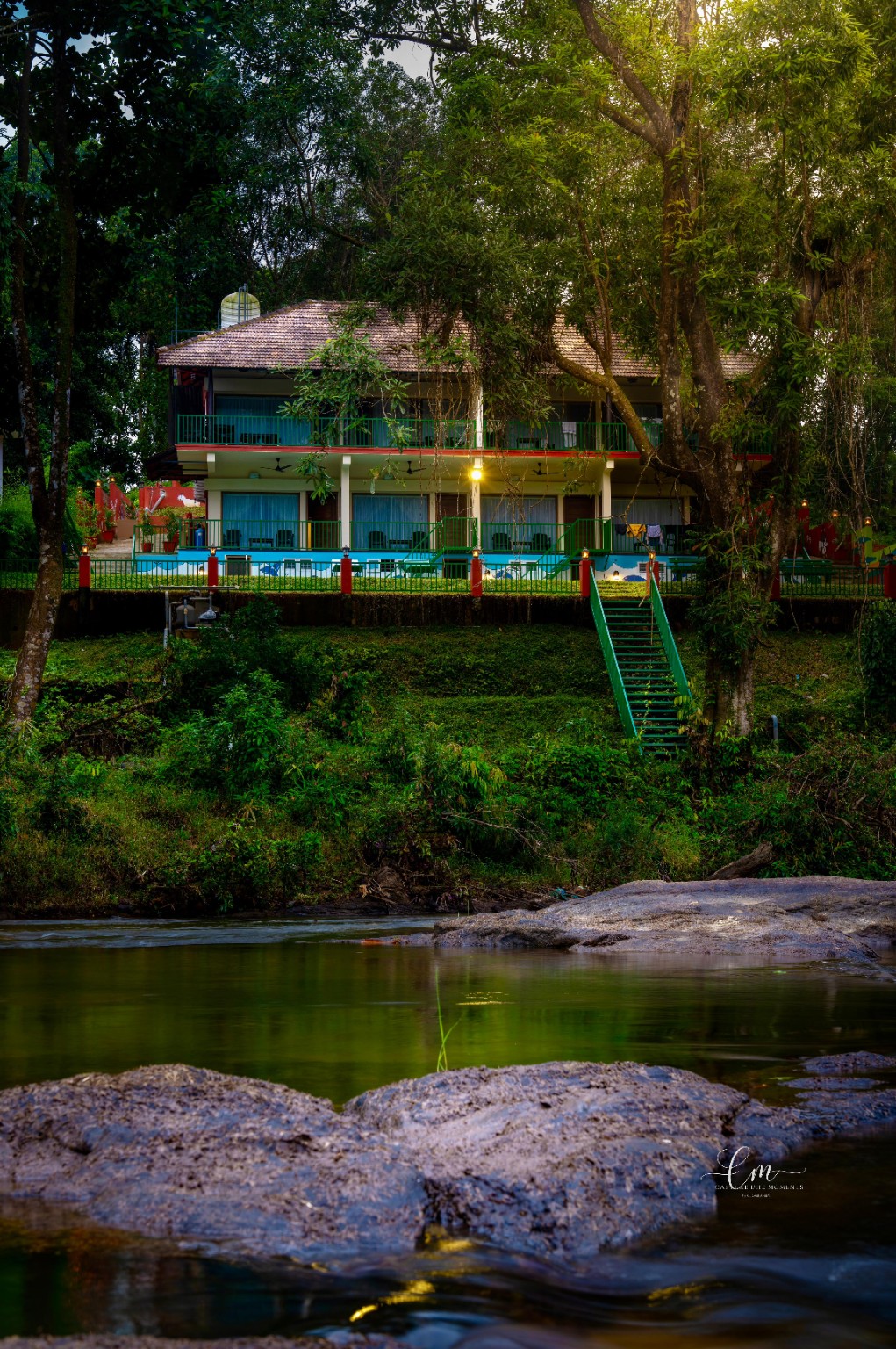 Falcon Riverview Resorts seen across the Pooyamkutty river, its balconied tiled-roof building framed by tall forest trees