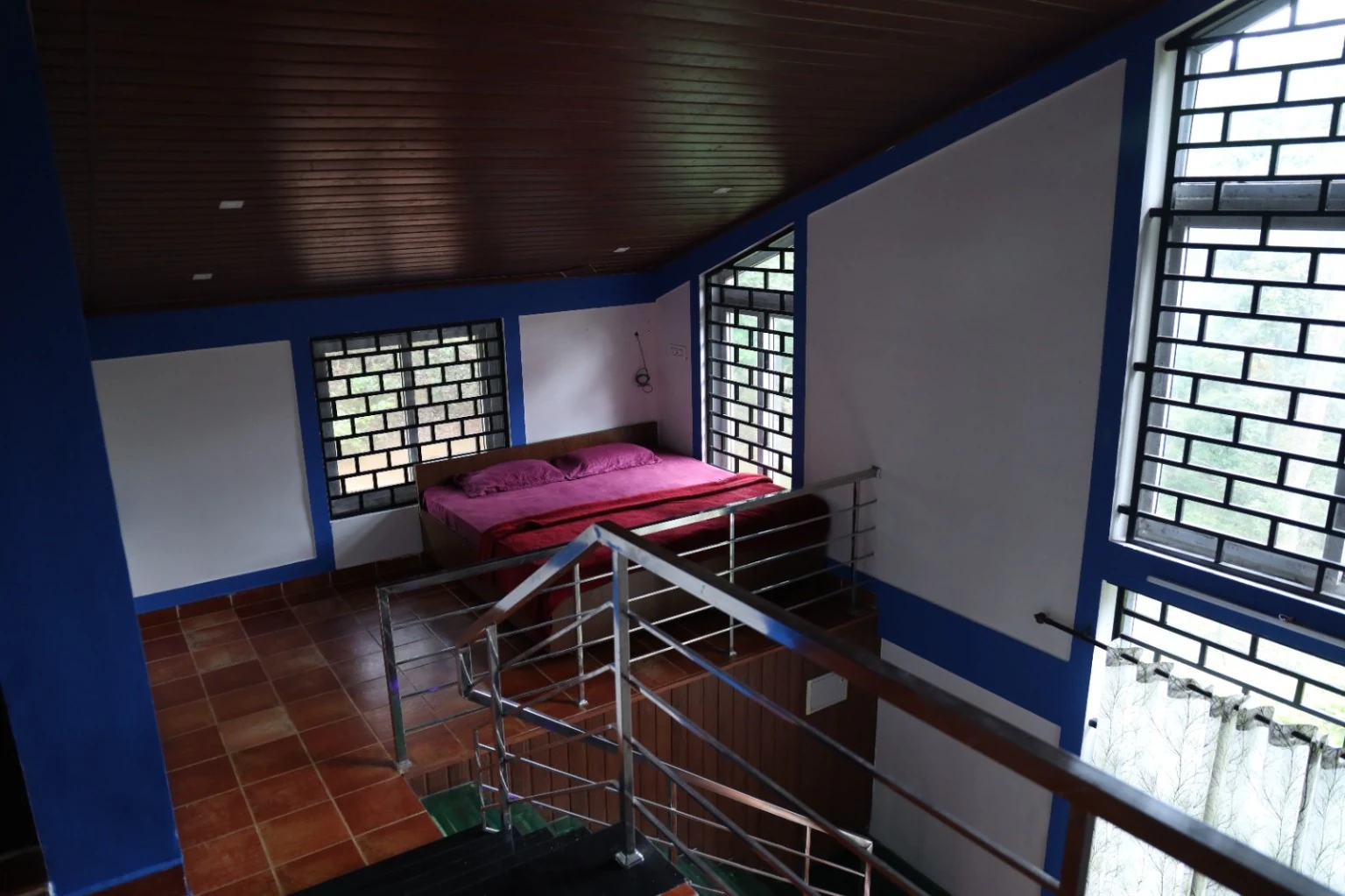 Bed beside the open upper landing with stairs, railings and windows