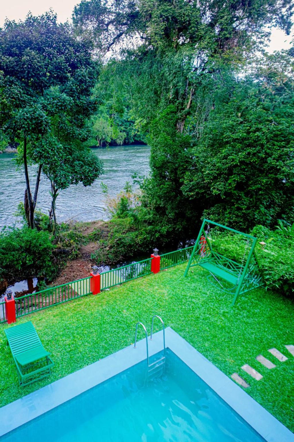 Garden pool and swing seat on the riverside lawn at Falcon Riverview Resorts, with the river flowing beyond the fence
