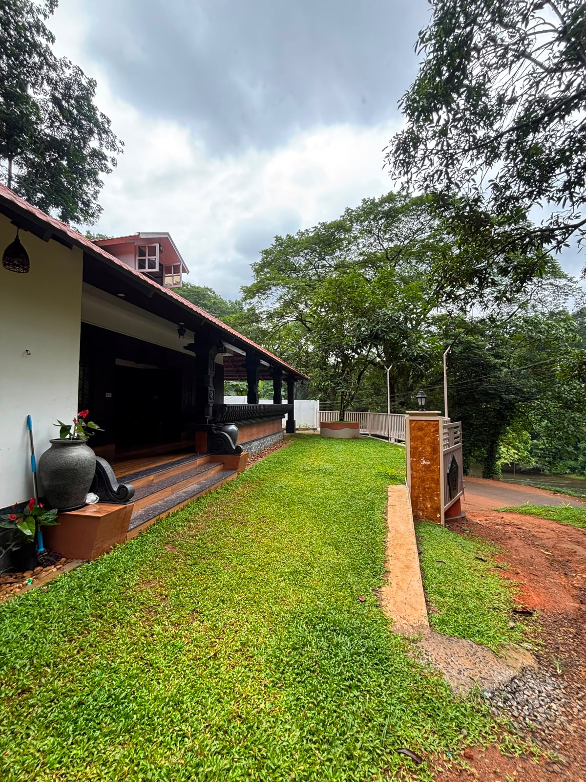 Ben & B's Stay in Pooyamkutty seen from the lawn, with a tiled-roof verandah, carved wooden pillars and forest beyond