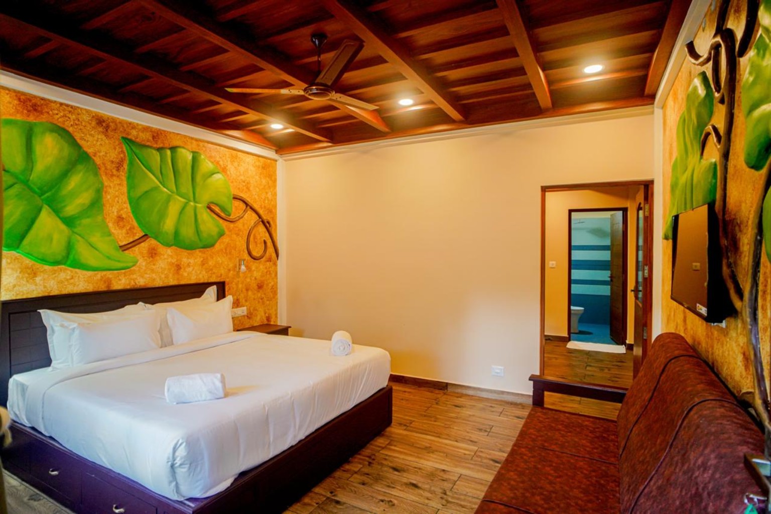 Spacious cottage bedroom with sculpted leaf wall art, seating area and ensuite bathroom beyond