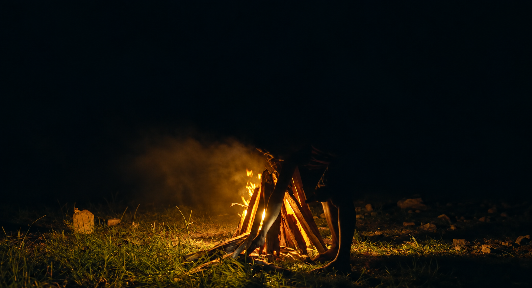 A campfire being carefully prepared after dark