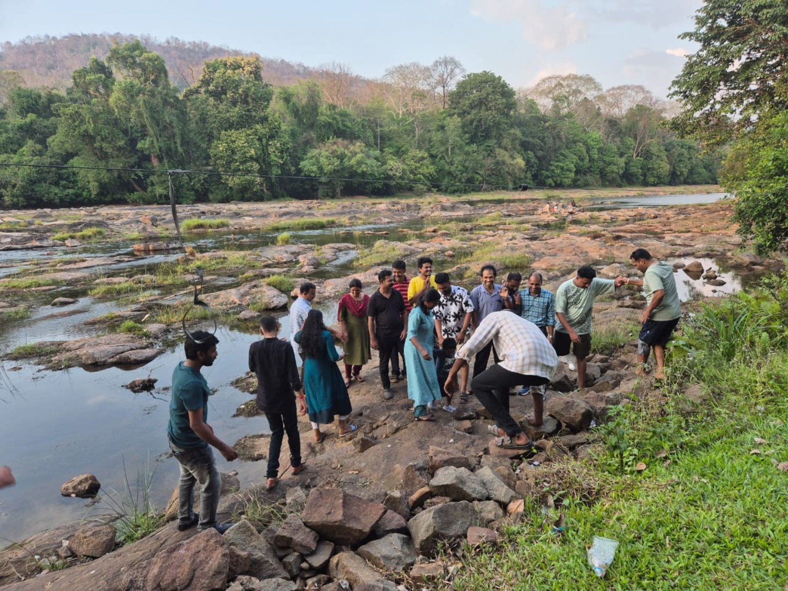 Travellers exploring a rocky riverbed with forested hills behind them