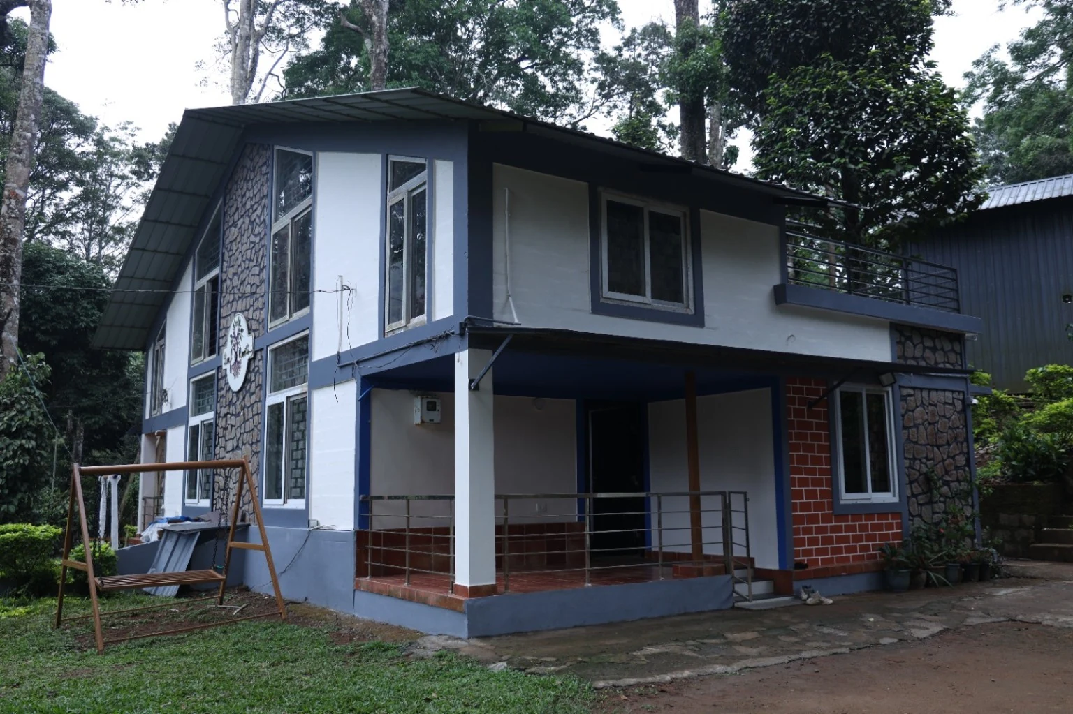 Broad front of the two-storey cottage with an outdoor staircase and covered sit-out